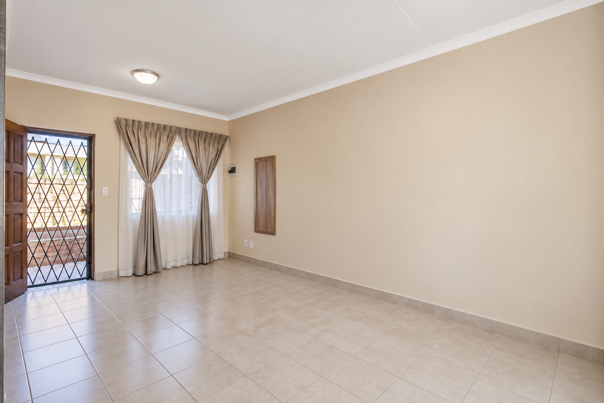 A bright and spacious living area featuring neutral tiled flooring, clean walls, and direct access to an outdoor space through a secure door.