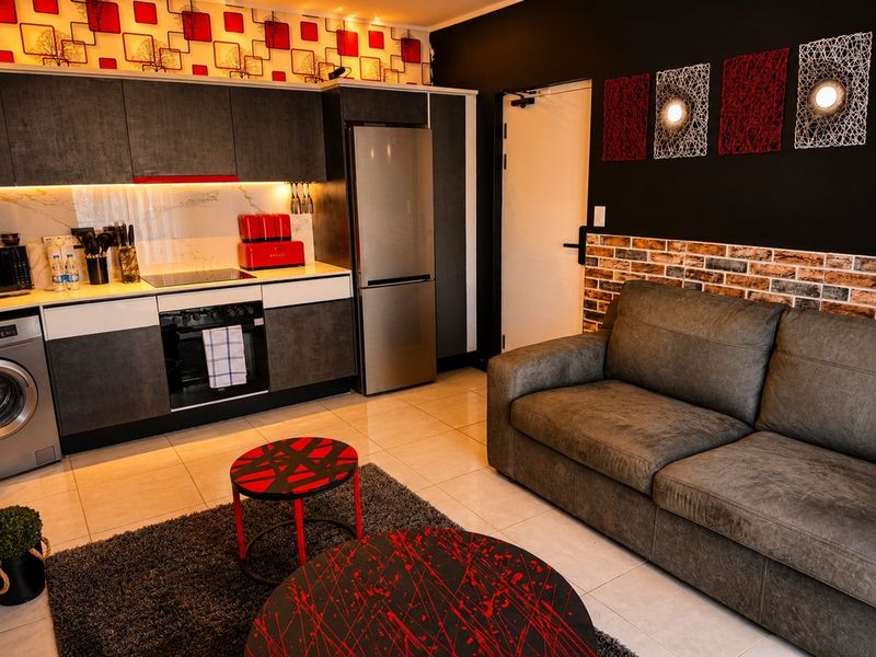 Modern open-plan apartment featuring a sleek kitchen with built-in appliances, stone-look backsplash, and a stylish exposed brick accent wall in the living area.