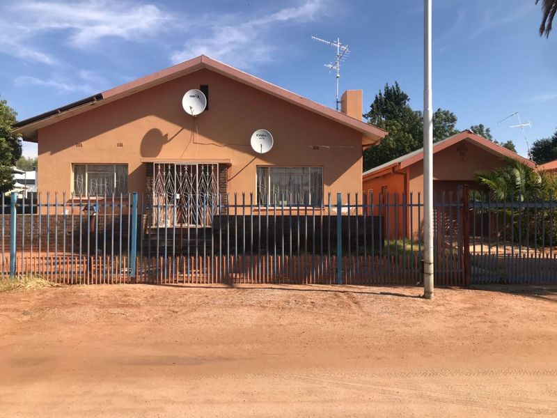Front view of a single-story house featuring a tiled roof, brick facade, security fencing, and an attached carport.