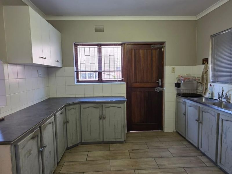 A functional kitchen featuring built-in cabinetry, laminate countertops, a double basin sink, and tiled splashbacks, offering a blank canvas for renovation.