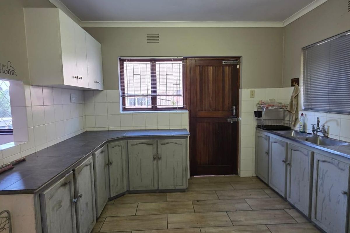 A functional kitchen featuring built-in cabinetry, laminate countertops, a double basin sink, and tiled splashbacks, offering a blank canvas for renovation.