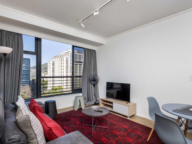 Bright open-plan living area featuring large windows with city views, modern track lighting, and elegant herringbone flooring.