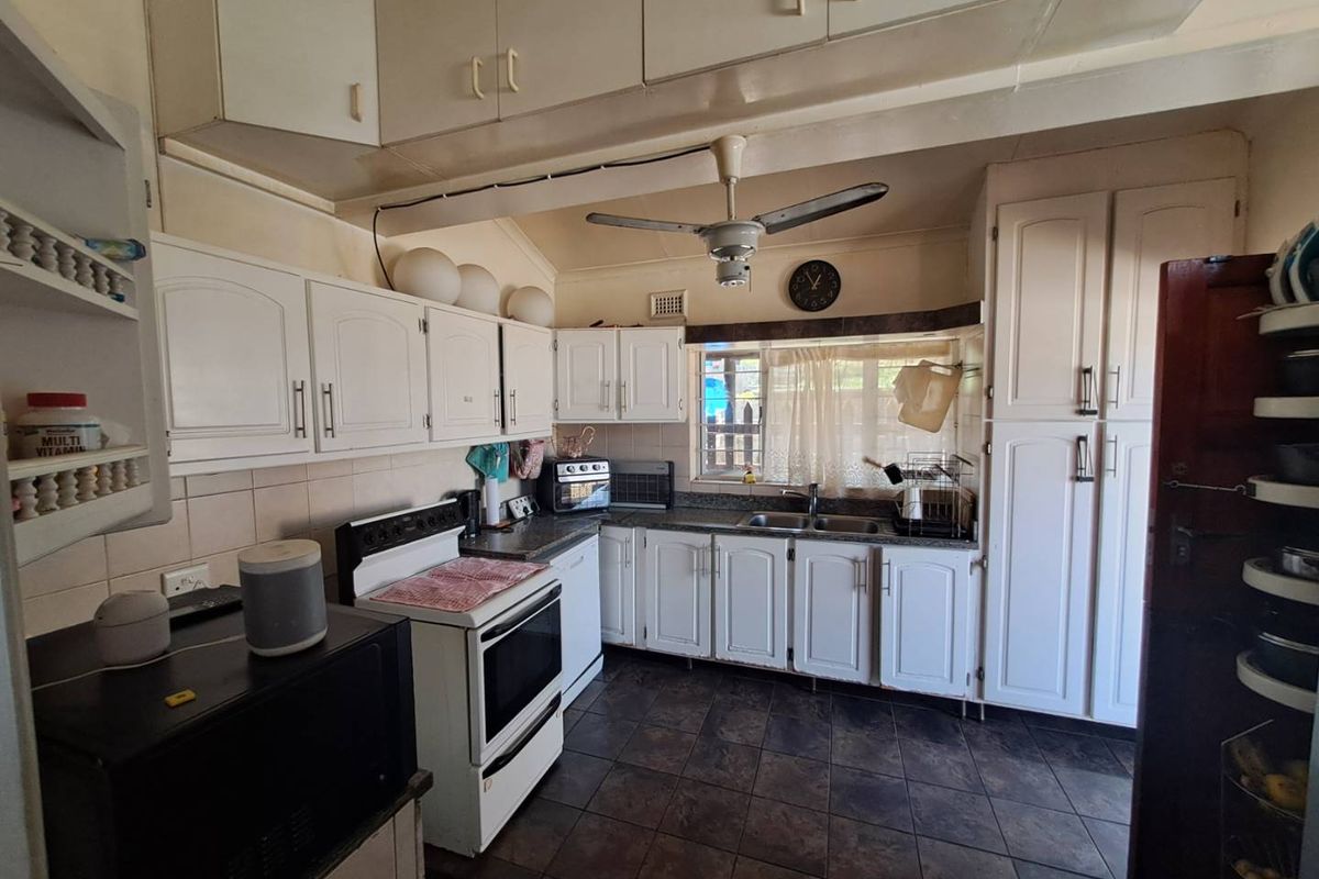 A functional kitchen featuring white cabinetry, a built-in stove, double sink, and dark tiled flooring, offering a practical layout for daily meal preparation.
