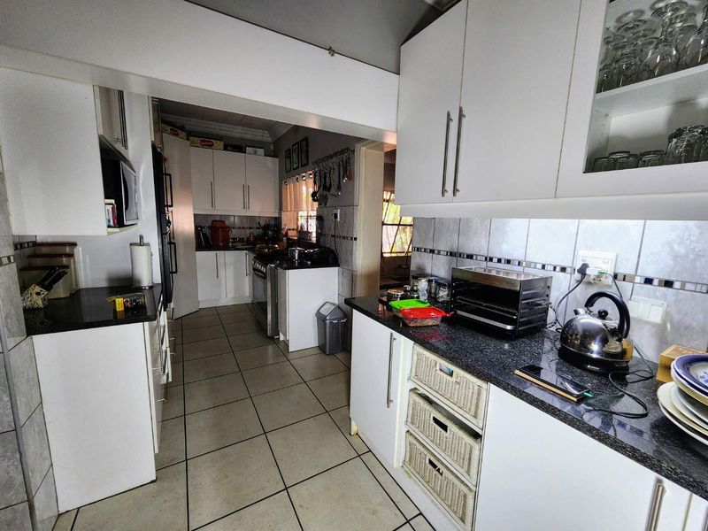 A functional kitchen featuring white cabinetry, dark granite countertops, and tiled flooring, offering a practical layout with ample storage space.