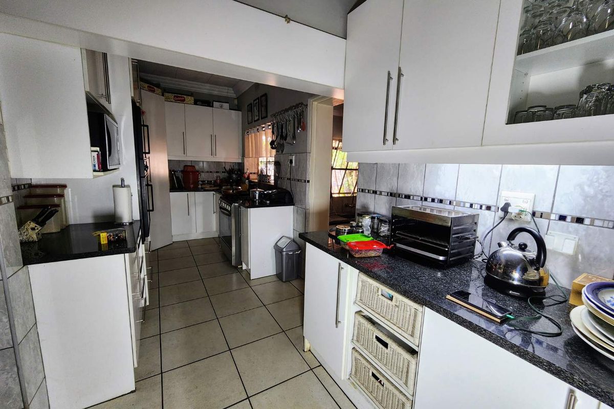 A functional kitchen featuring white cabinetry, dark granite countertops, and tiled flooring, offering a practical layout with ample storage space.