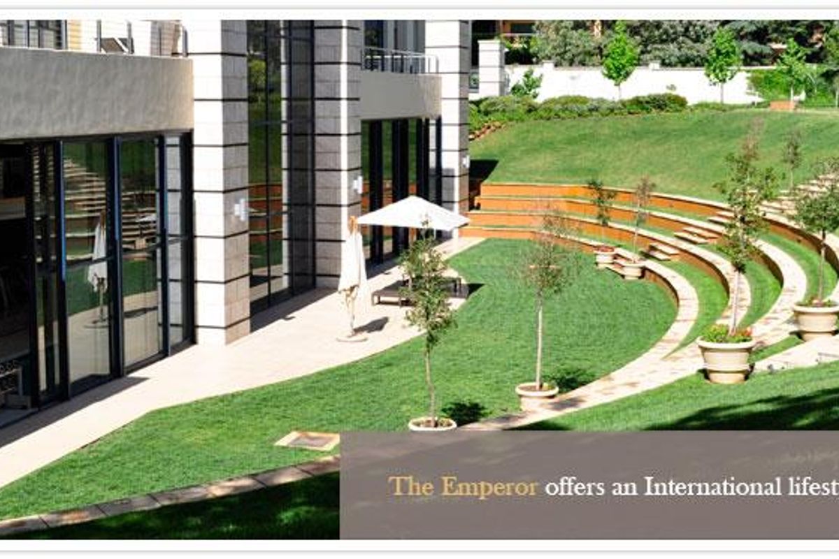A beautifully landscaped rear garden featuring tiered grass terraces, stone retaining walls, and a paved patio area adjacent to the apartment building.