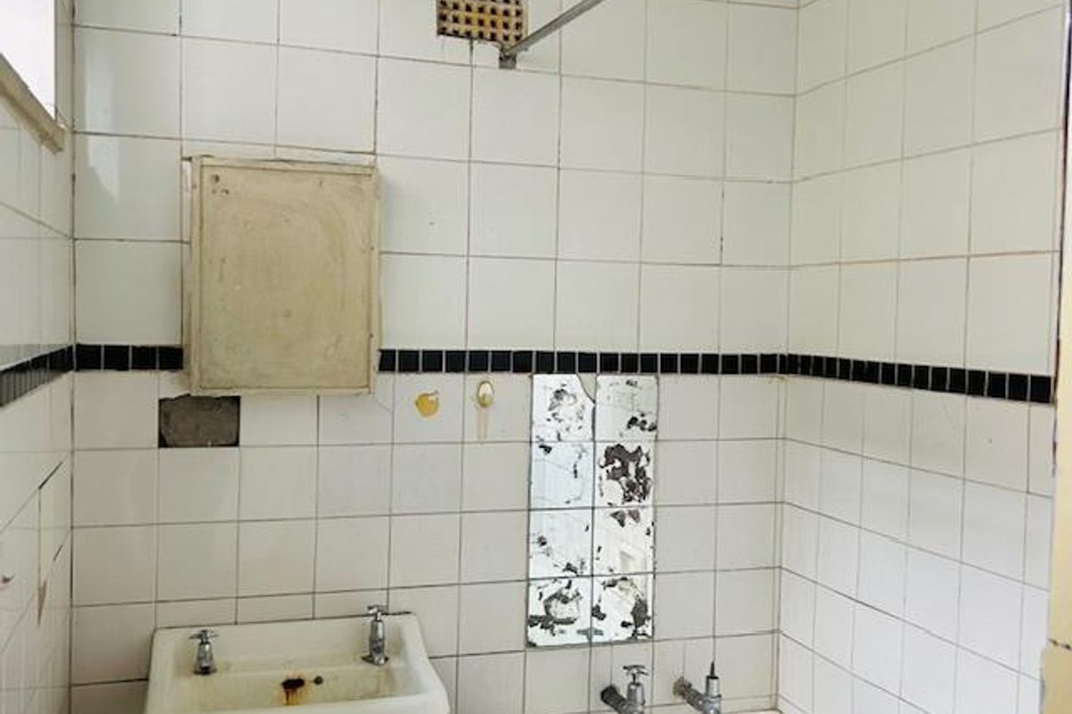 A dated bathroom featuring original white wall tiles with black accents, a wall-mounted basin, and a built-in bathtub requiring significant renovation.