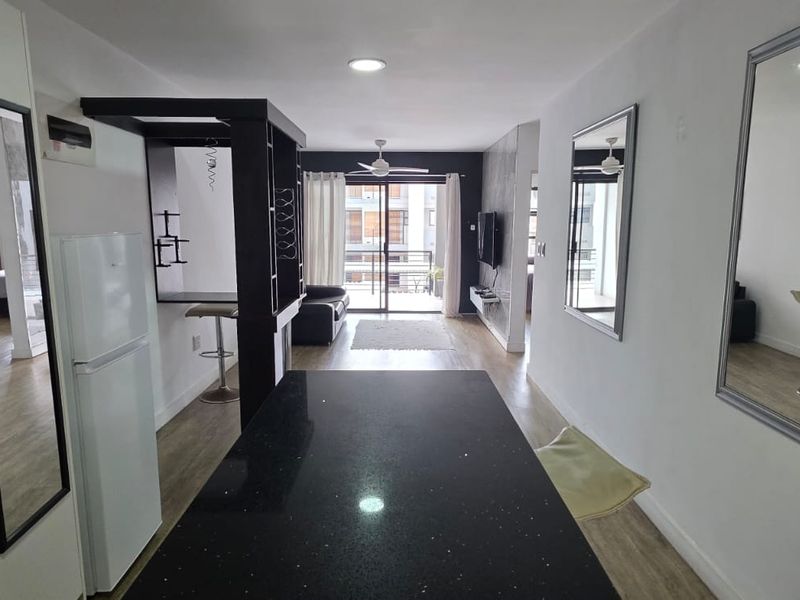 Open-plan living area featuring a central breakfast bar, laminate flooring, recessed lighting, and direct access to a private balcony.