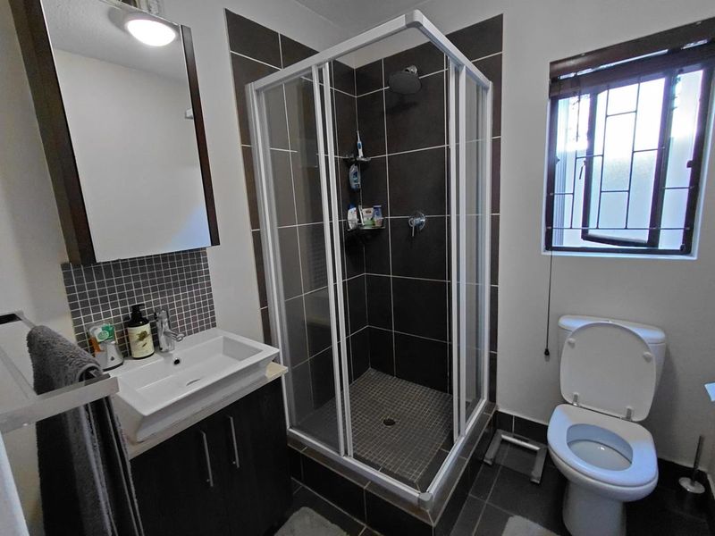 A modern bathroom featuring a glass shower enclosure, vanity basin, and toilet, finished with dark floor and wall tiling.