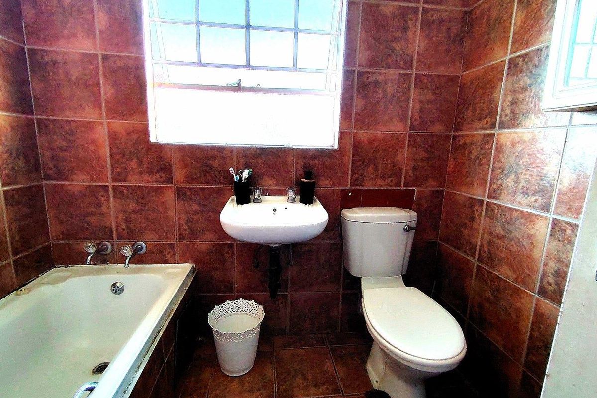 A compact bathroom featuring a bathtub, wall-mounted basin, and toilet, finished with dark, dated ceramic wall and floor tiles.