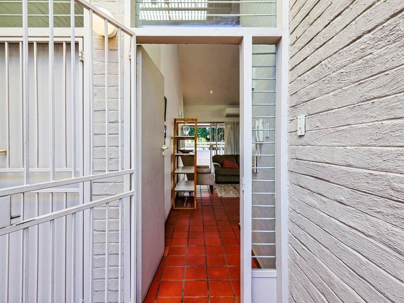 Entrance hallway featuring terracotta floor tiles, painted brick walls, and a security gate, leading into the main living area.