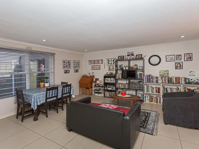 A spacious living area featuring neutral tiled flooring, recessed downlighting, and large windows fitted with venetian blinds.