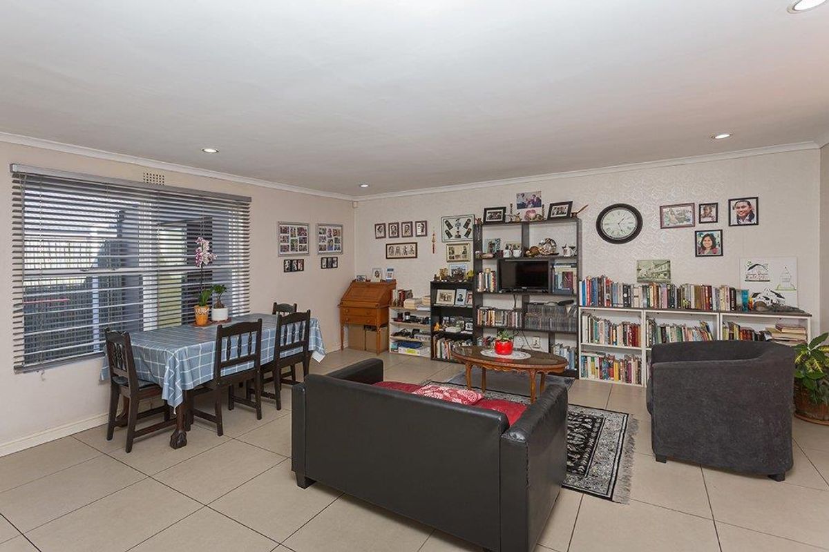A spacious living area featuring neutral tiled flooring, recessed downlighting, and large windows fitted with venetian blinds.