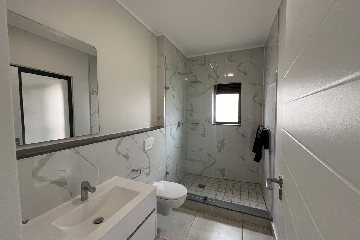 Modern bathroom featuring a walk-in shower with glass enclosure, wall-mounted toilet, and a sleek vanity with a mirror.
