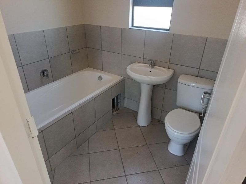 A functional bathroom featuring a pedestal basin, toilet, and a tiled bathtub with a missing apron tile.