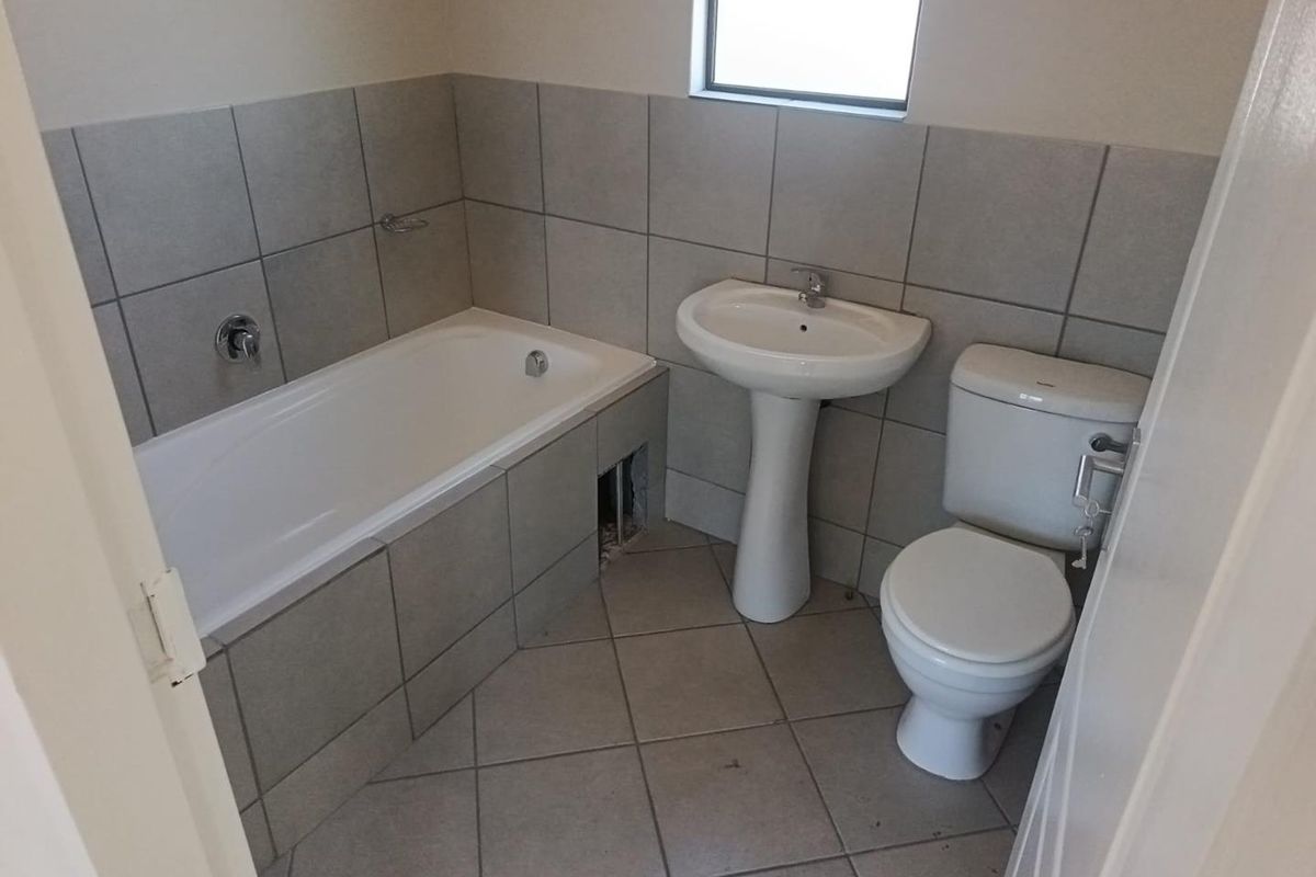 A functional bathroom featuring a pedestal basin, toilet, and a tiled bathtub with a missing apron tile.