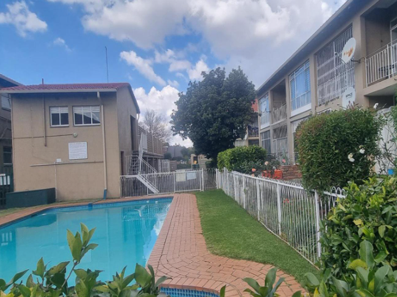 Communal swimming pool area featuring brick paving, metal fencing, and views of the townhouse complex exterior.