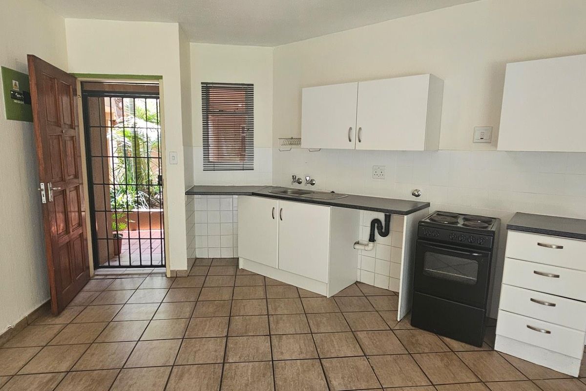 A functional kitchen area featuring white cabinetry, dark countertops, a freestanding stove, and direct access to an outdoor patio area.