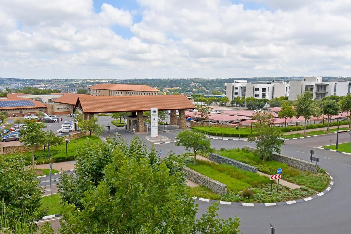 An elevated aerial view of the estate entrance, featuring landscaped gardens, paved roadways, and surrounding apartment complex infrastructure.