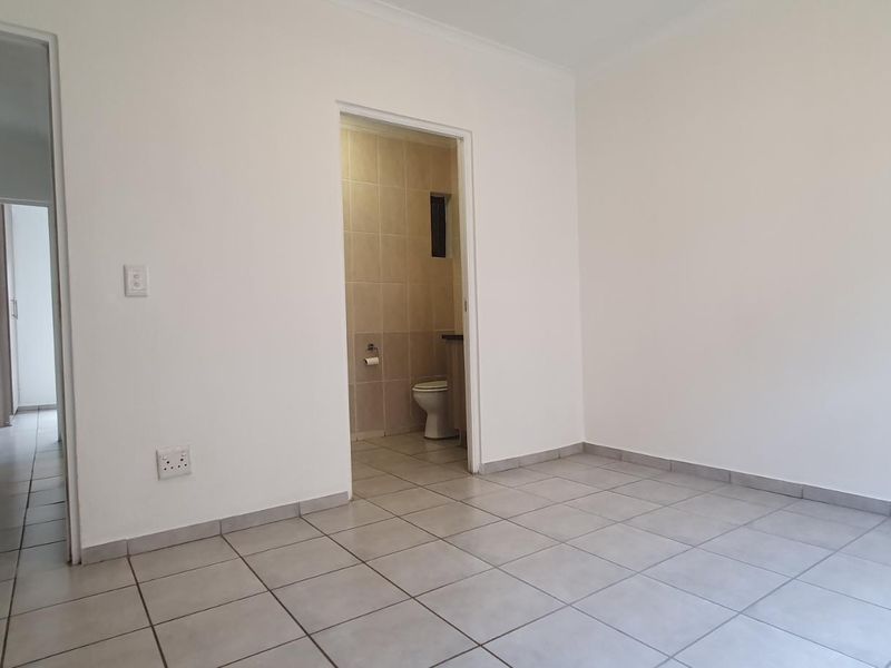 A clean, empty bedroom featuring neutral ceramic floor tiles, built-in storage, and direct access to an en-suite bathroom.