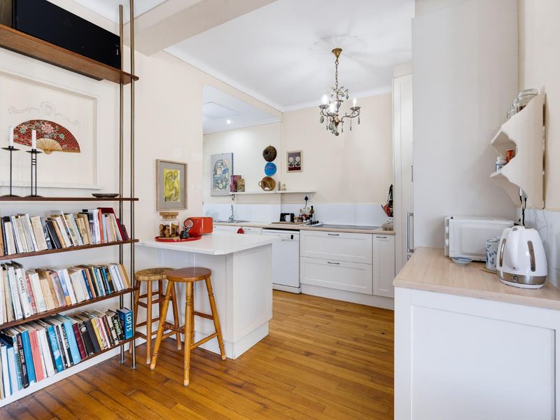 A bright, well-maintained kitchen featuring white cabinetry, light wood countertops, hardwood flooring, and a classic chandelier, offering a clean and functional cooking space.