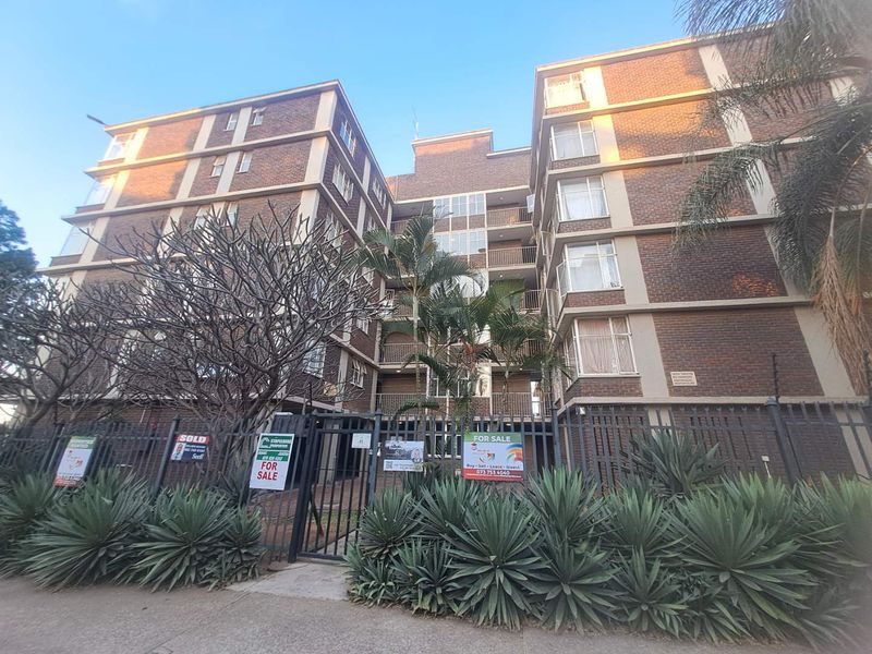 Exterior view of a multi-story brick apartment building featuring balconies, secure perimeter fencing, and gated access.