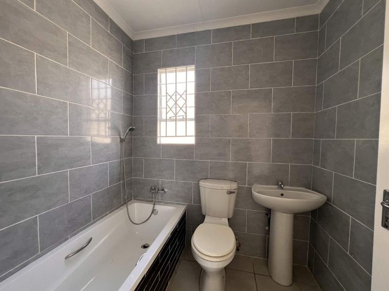 A clean, functional bathroom featuring grey wall tiles, a standard bathtub with shower attachment, a pedestal basin, and a toilet.
