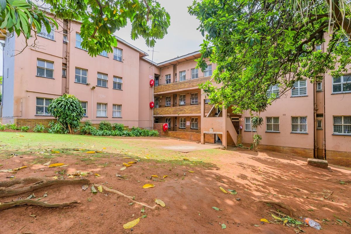 Rear view of the apartment complex showing the building facade, communal garden area, and external staircase access.