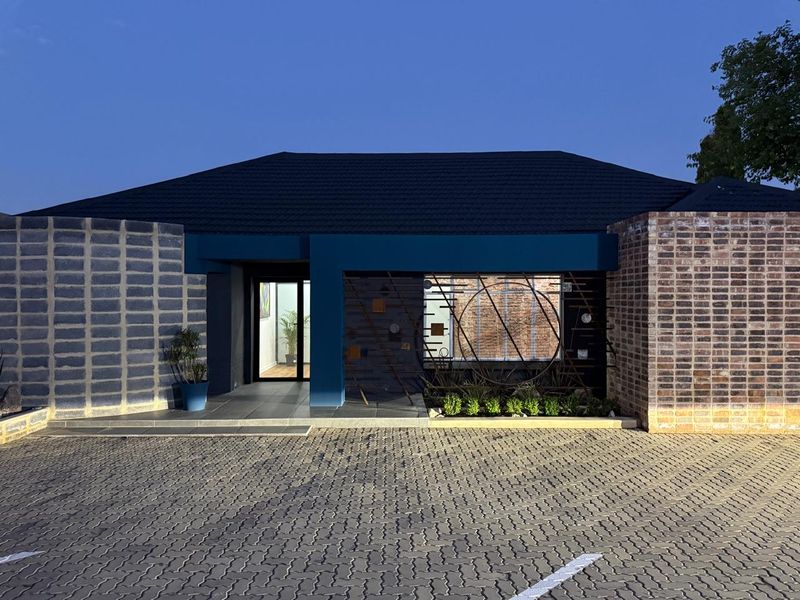 Modern commercial building facade featuring a combination of brick and concrete block textures, a dark tiled roof, and a paved parking area.