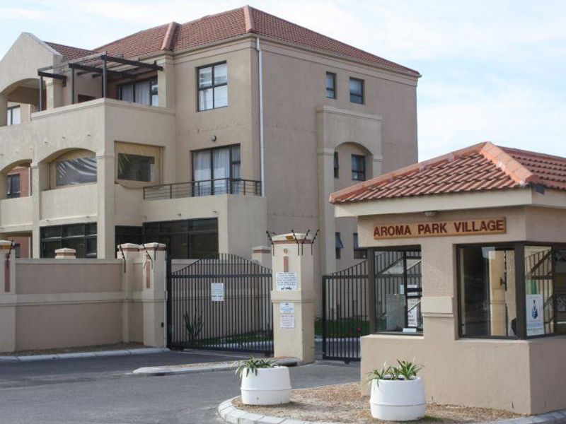 Front entrance view of Aroma Park Village apartment complex featuring a security gate, guard house, and multi-story residential building with balconies.