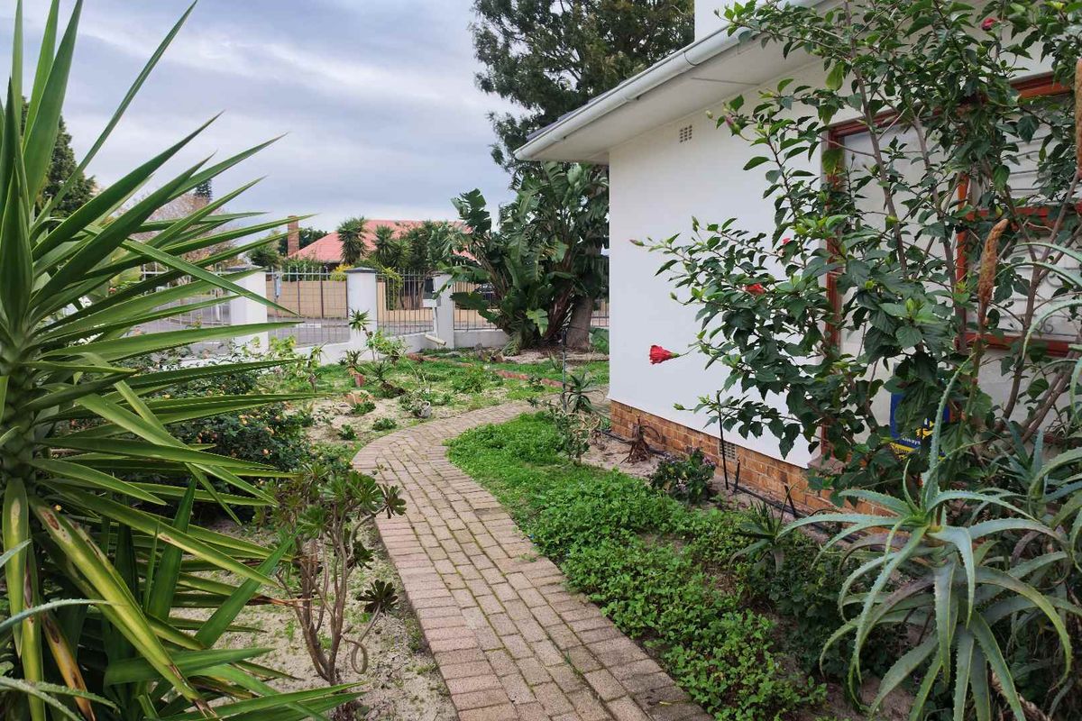 A side garden area featuring a brick paved pathway leading along the side of the house, bordered by established shrubs and a perimeter wall.
