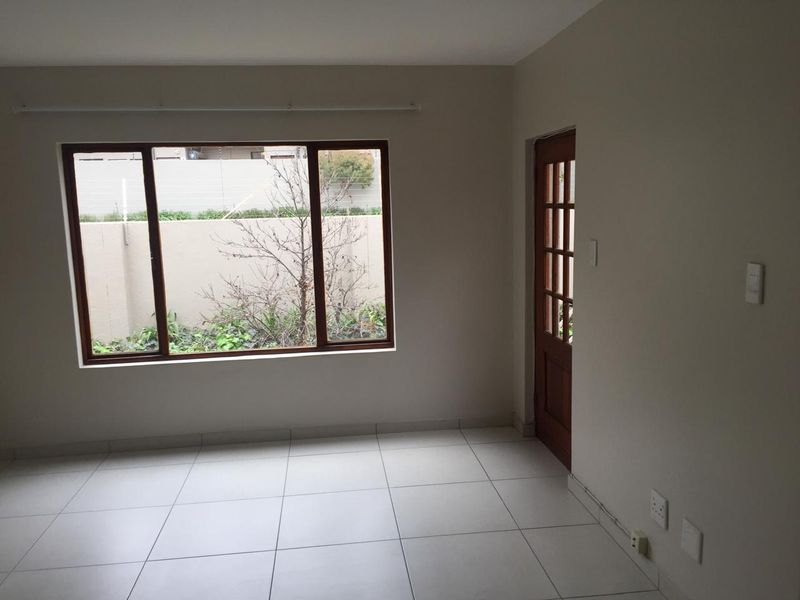 A bright, empty living area featuring neutral tiled flooring, a large timber-framed window, and a classic timber-framed glass door leading outdoors.
