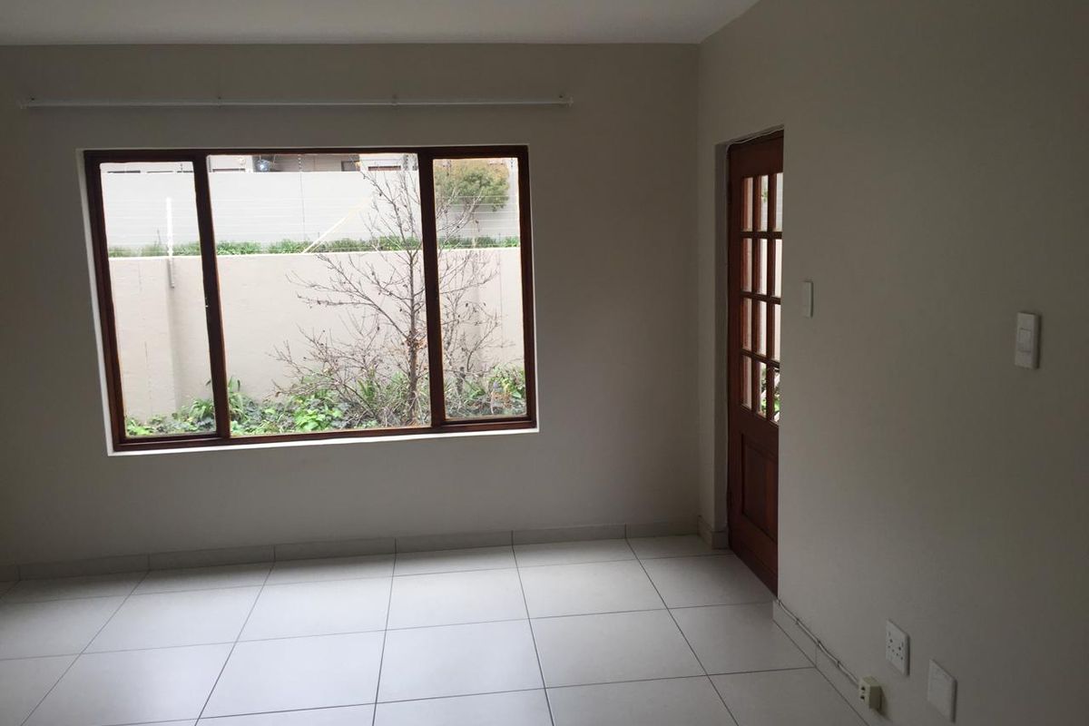 A bright, empty living area featuring neutral tiled flooring, a large timber-framed window, and a classic timber-framed glass door leading outdoors.