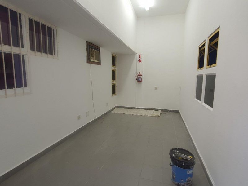 A clean, empty utility space featuring tiled flooring, security bars on windows, and a wall-mounted air conditioning unit.