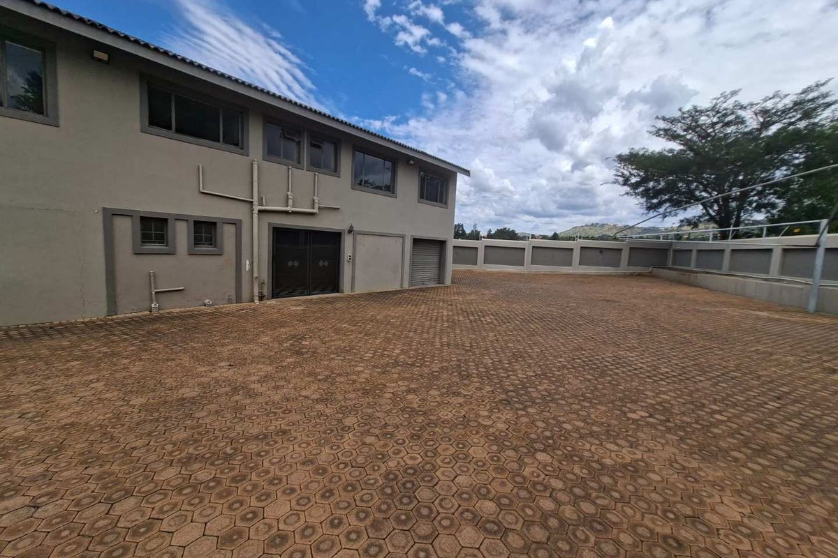 Spacious paved rear exterior area featuring a perimeter wall and access to the building via a roller shutter door.