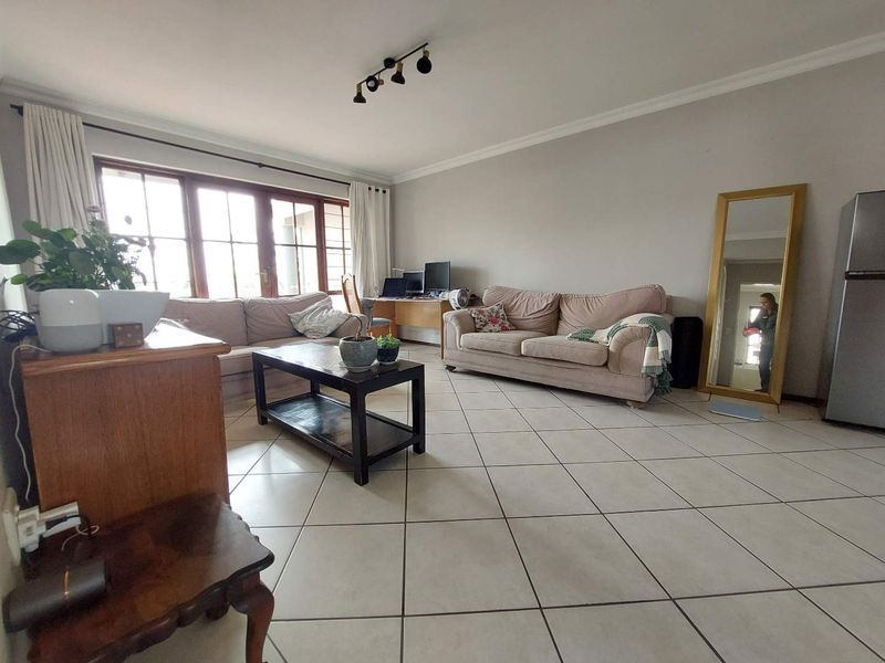 A spacious living room featuring neutral tiled flooring, large windows allowing natural light, and ceiling-mounted track lighting.