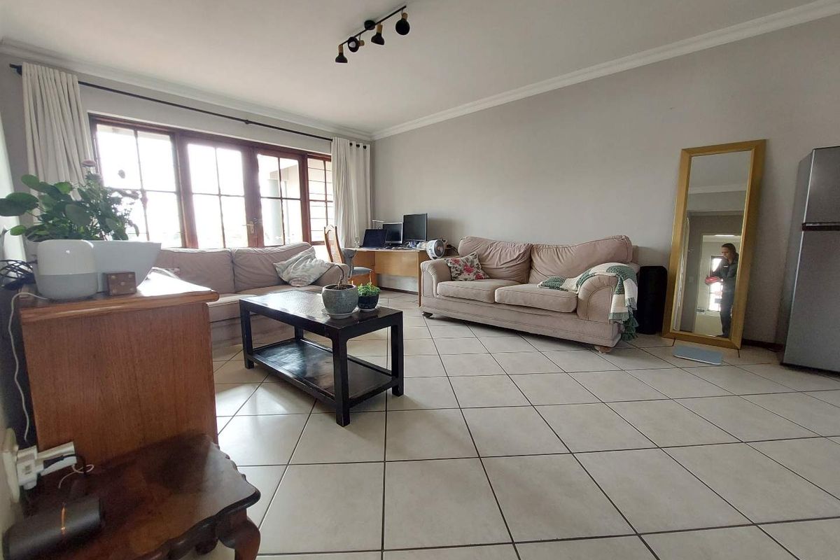 A spacious living room featuring neutral tiled flooring, large windows allowing natural light, and ceiling-mounted track lighting.