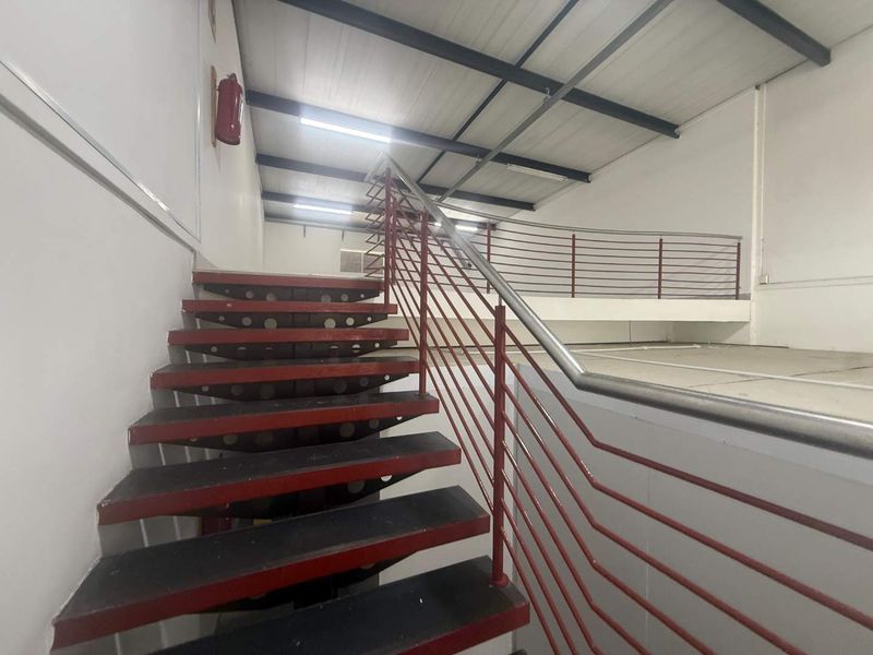 Industrial utility space featuring a metal staircase leading to an open mezzanine level with exposed steel beams and functional safety fixtures.