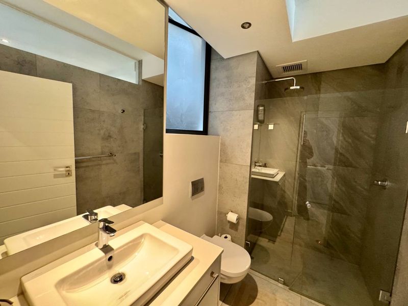 Modern bathroom featuring a glass-enclosed shower with rain head, wall-mounted toilet, vanity basin, and large mirror with contemporary grey tiling.