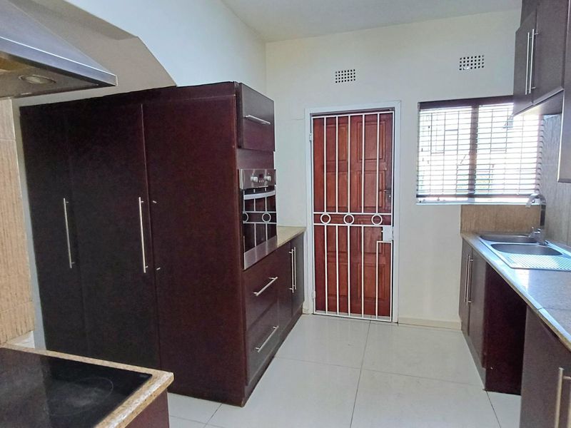 A functional kitchen featuring dark wood cabinetry, built-in oven, electric hob, extractor fan, and tiled flooring with a secure exterior door.