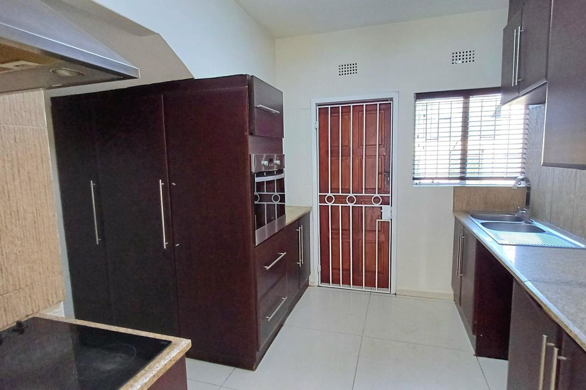 A functional kitchen featuring dark wood cabinetry, built-in oven, electric hob, extractor fan, and tiled flooring with a secure exterior door.