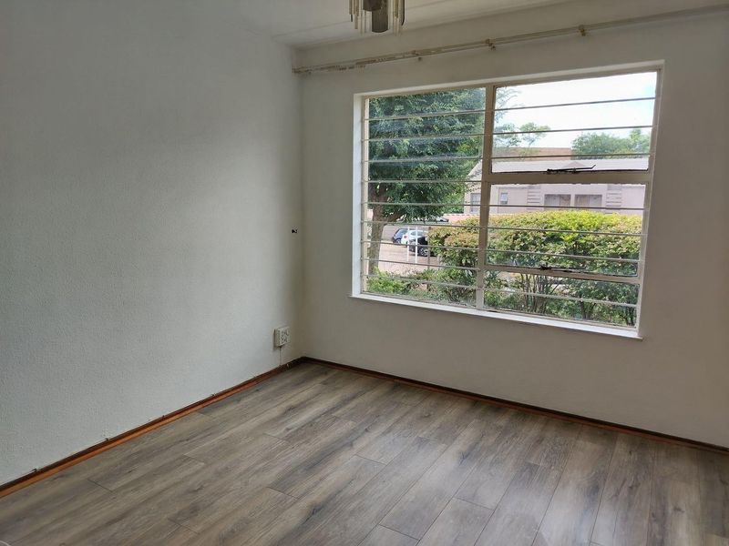 A bright, empty bedroom featuring modern laminate flooring, large windows with security bars, and neutral wall finishes, ready for personalization.