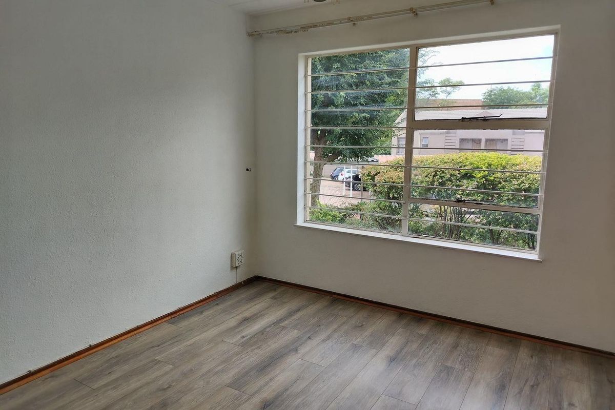 A bright, empty bedroom featuring modern laminate flooring, large windows with security bars, and neutral wall finishes, ready for personalization.