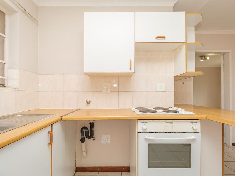 A functional kitchen featuring white cabinetry, laminate countertops, a built-in electric oven and stove, and tiled backsplash, currently in need of cosmetic updates.
