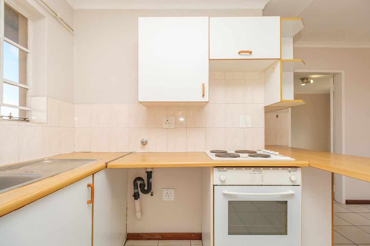 A functional kitchen featuring white cabinetry, laminate countertops, a built-in electric oven and stove, and tiled backsplash, currently in need of cosmetic updates.