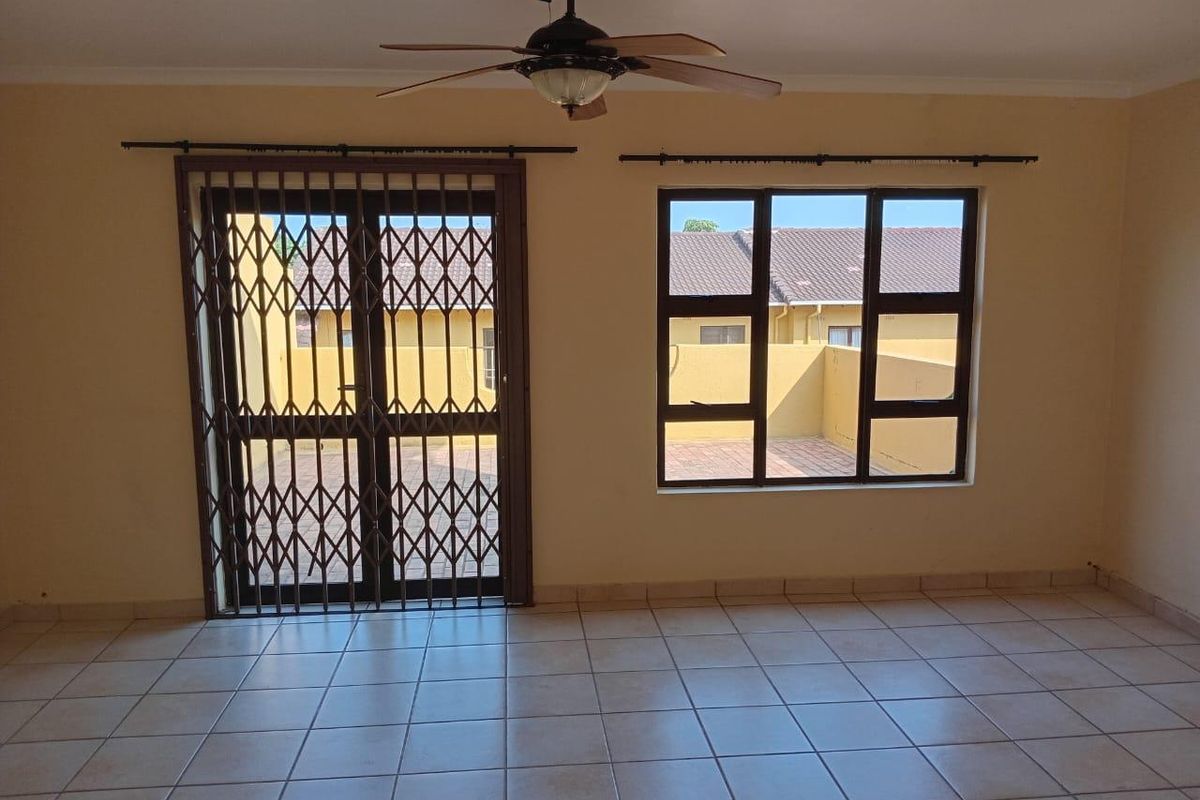 A spacious living area featuring ceramic floor tiles, a ceiling fan, and security gates leading to an outdoor patio space.
