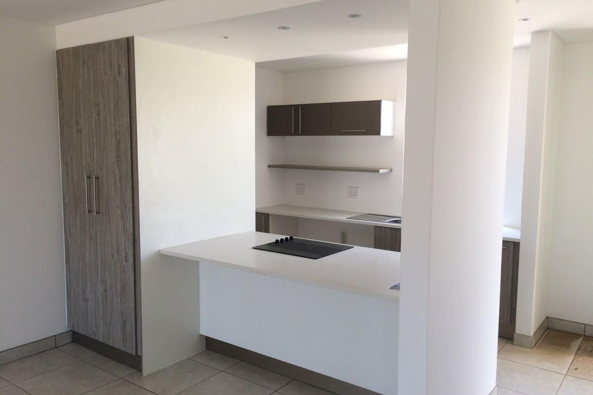 Modern open-plan kitchen featuring a central island with a built-in hob, sleek cabinetry, and neutral tiled flooring.