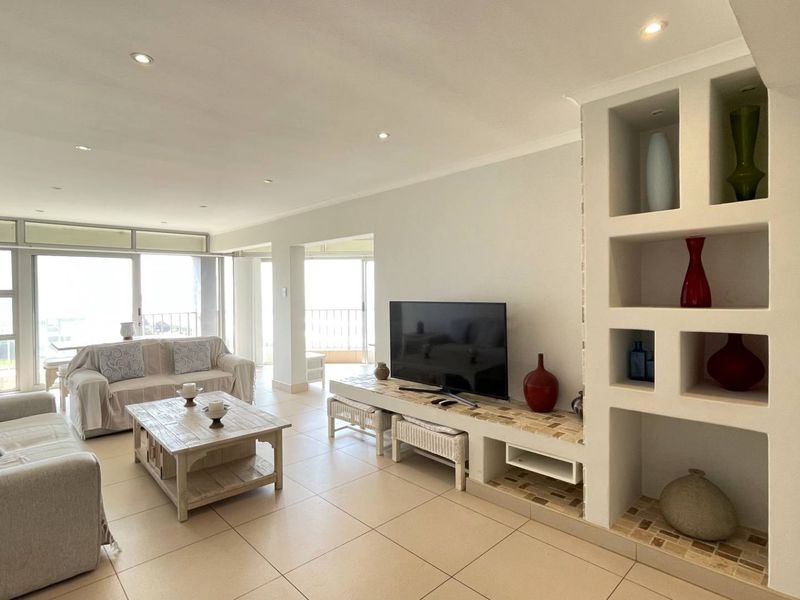 Spacious living room featuring tiled flooring, recessed lighting, and a custom built-in shelving unit, with direct access to a balcony through sliding glass doors.