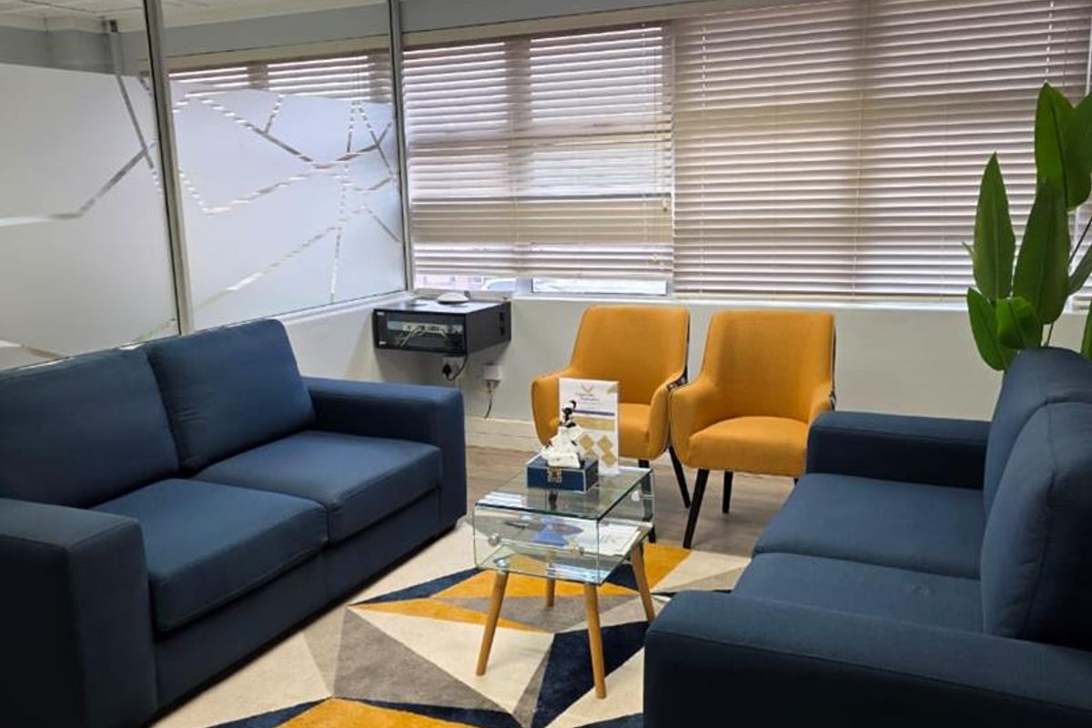 A professional office space featuring a glass partition wall, venetian blinds, recessed lighting, and durable laminate flooring.