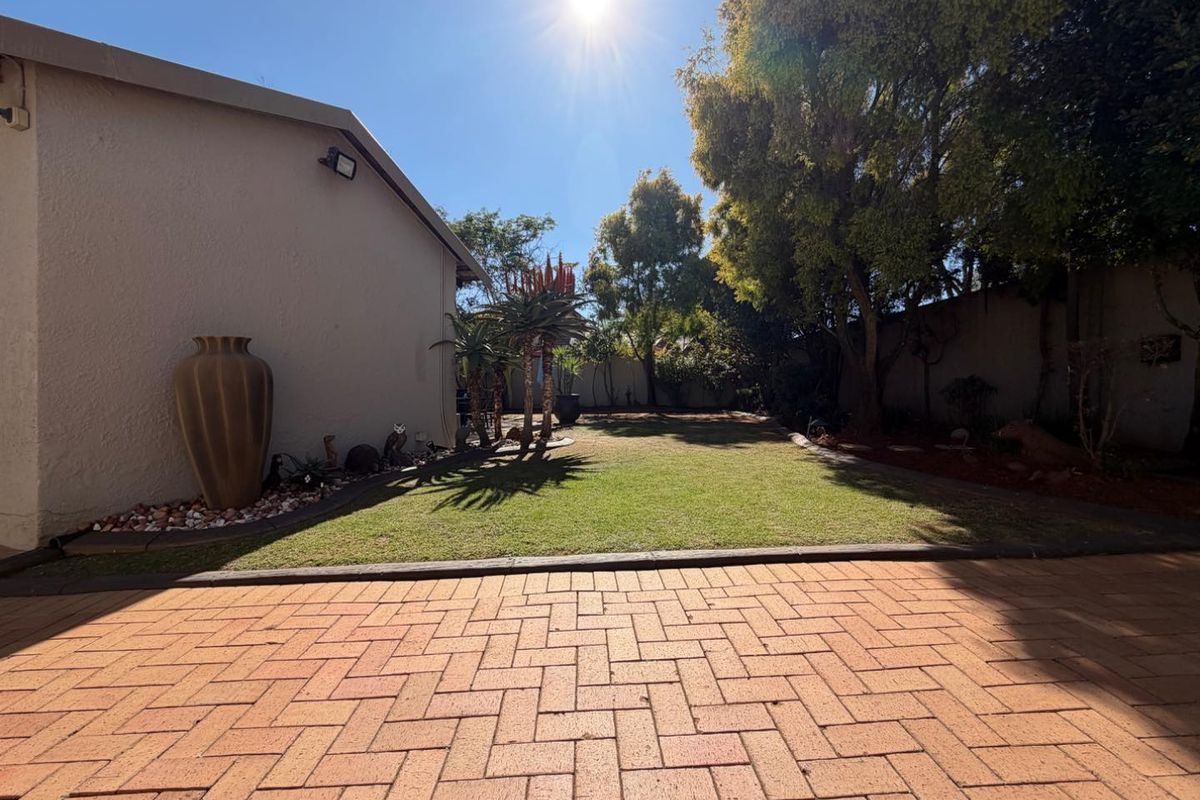 A well-maintained rear garden featuring a brick-paved patio area, established lawn, and perimeter walling, providing a private outdoor space.